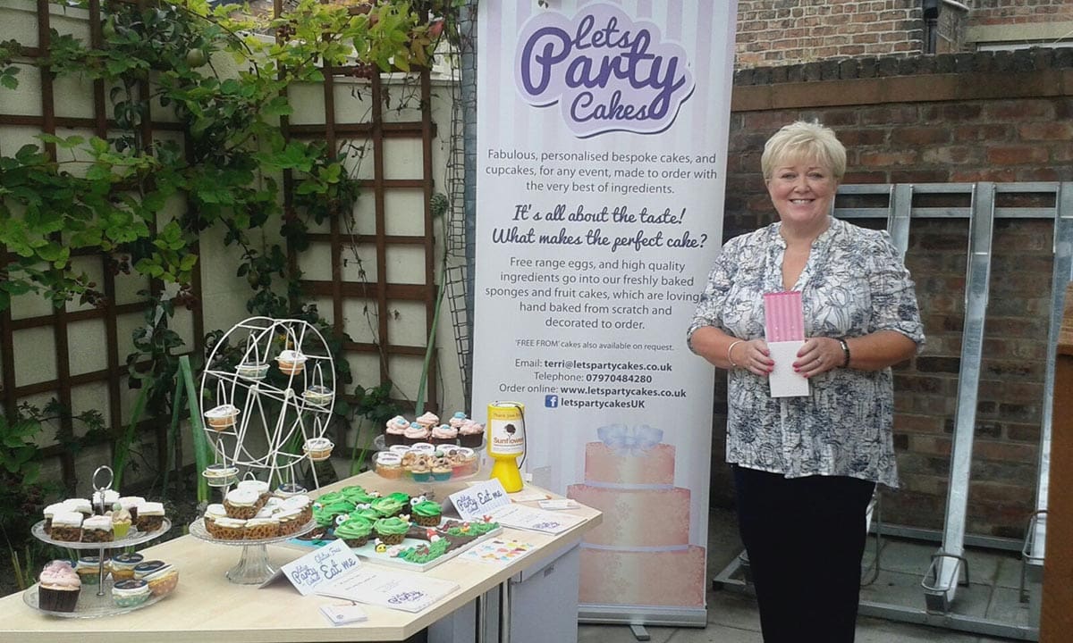 Photograph of mum standing beside a pull up banner with information about 'Lets Party Cakes'